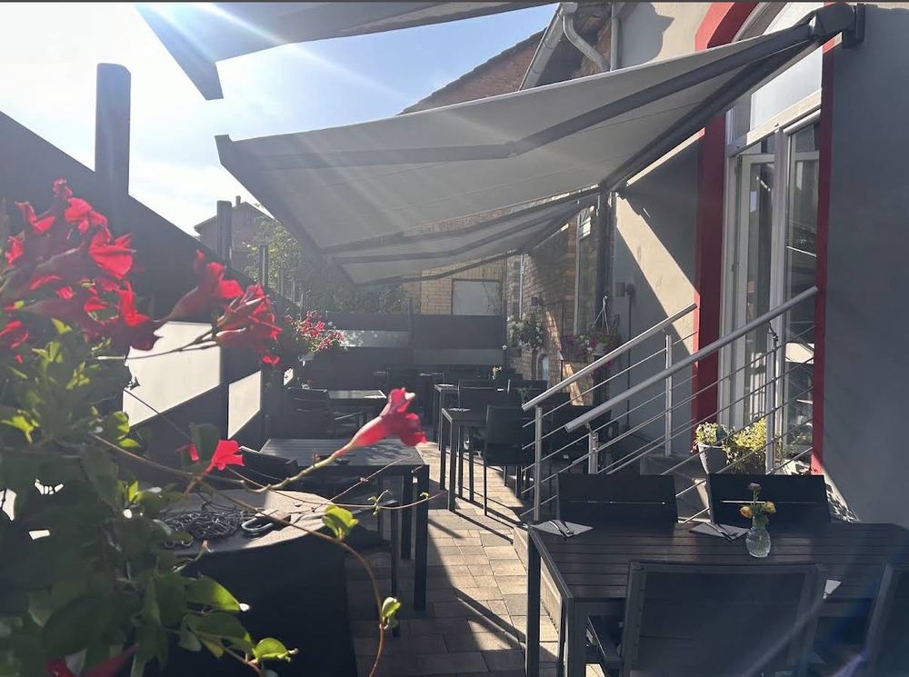 Die Terrasse des El Greco mit Markise und Blumen an einem Sommertag